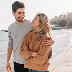 Para rozmawia na plaży. On obejmuje ją ramieniem, ona patrzy na niego z uśmiechem. Może to być inspiracja, jak rozkochać introwertyka.