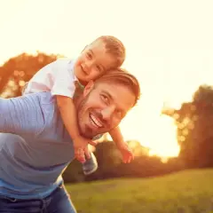 Szczęśliwy tata niesie syna na barana podczas zachodu słońca.