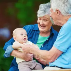 Uśmiechnięta babcia trzyma wnuka, dziadek patrzy na dziecko. To jest babcia, która kocha swoje wnuki.