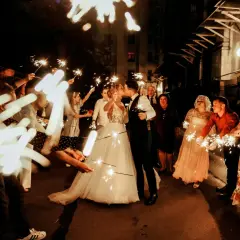 Para co zamiast zimnych ogni na weselu? Para młoda całuje się wśród gości trzymających zimne ognie, tworząc magiczną atmosferę.