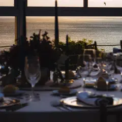 Elegancko nakryty stół na przyjęcie nad morzem. W tle zachód słońca i morze. To może być wesele bez alkoholu, gdzie liczy się wspólna radość i piękno chwili.