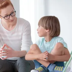 Kobieta w okularach uważnie słucha chłopca. Pokazuje, jak rozmawiać z dzieckiem, budując zaufanie i zrozumienie.