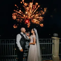 Para młoda wznosi toast na tle spektakularnych fajerwerków na wesele. Pozwolenie na ten pokaz było kluczowe dla tej magicznej chwili.