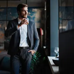 Elegancki mężczyzna w garniturze, z drinkiem w dłoni, zastanawia się, maczo kto to.