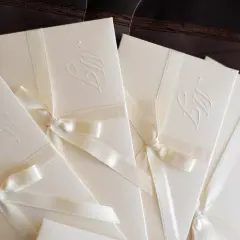 Eleganckie zaproszenia z monogramem i satynową wstążką, gotowe do wręczenia jako zaproszenie z osobą towarzyszącą.