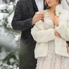 Para młoda w zimowej scenerii. Ona w białym futerku i sukni ślubnej, on w eleganckim płaszczu. Ich ślub zimą jest pełen uroku.