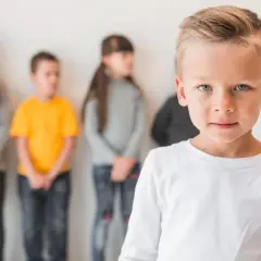 Chłopiec na pierwszym planie, z tyłu inne dzieci. Obraz symbolizuje problemy nastolatków w relacjach z rówieśnikami, poczucie wyobcowania.