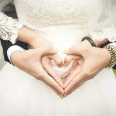 Dłonie tworzą serce, symbol miłości przed ślubem cywilnym. Panna młoda w koronkowej sukni i pan młody w garniturze.