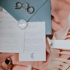 Eleganckie zaproszenia ślubne z pieczęcią i obrączkami. Widać fragmenty tekstu, które pomagają zrozumieć, jak wypisać zaproszenia na uroczystość.
