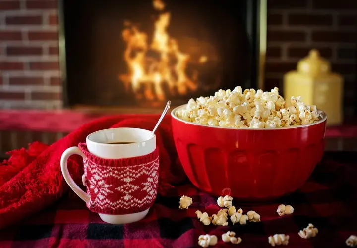 Idealne pomysły na randkę w domu: kubek gorącej czekolady, miska popcornu i przytulny koc przy kominku.