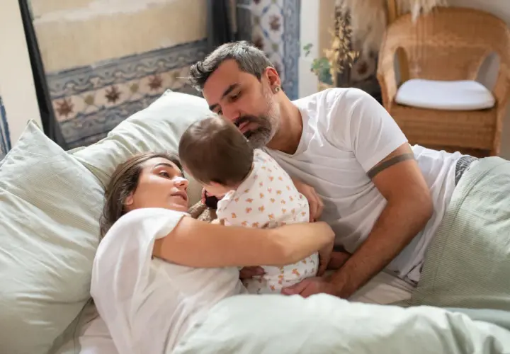 Rodzice tulą dziecko w łóżku. Bliskość i czułość w rodzinnym spaniu z dzieckiem to ważny aspekt psychologii rozwoju.