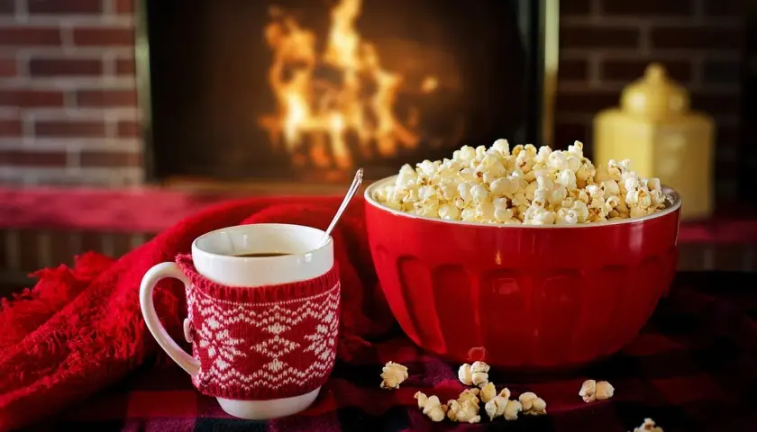 Idealne pomysły na randkę w domu: kubek gorącej czekolady, miska popcornu i przytulny koc przy kominku.