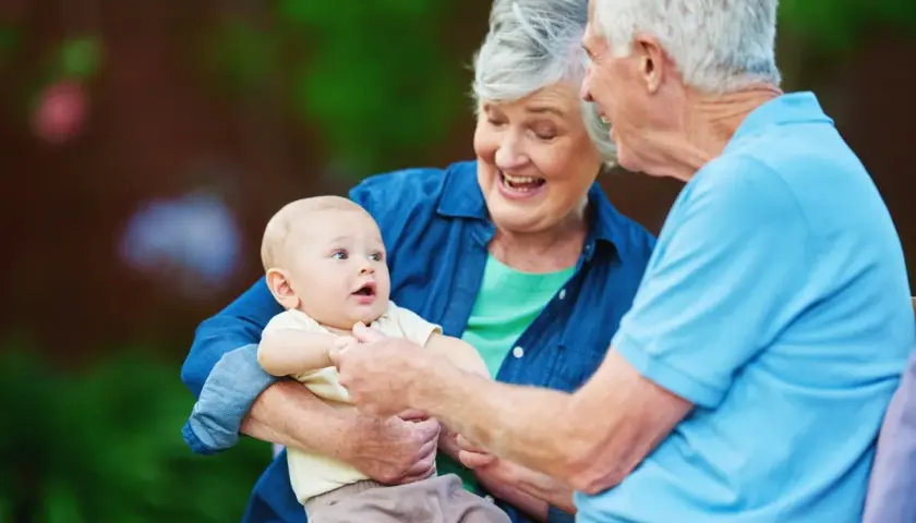 Uśmiechnięta babcia trzyma wnuka, dziadek patrzy na dziecko. To jest babcia, która kocha swoje wnuki.
