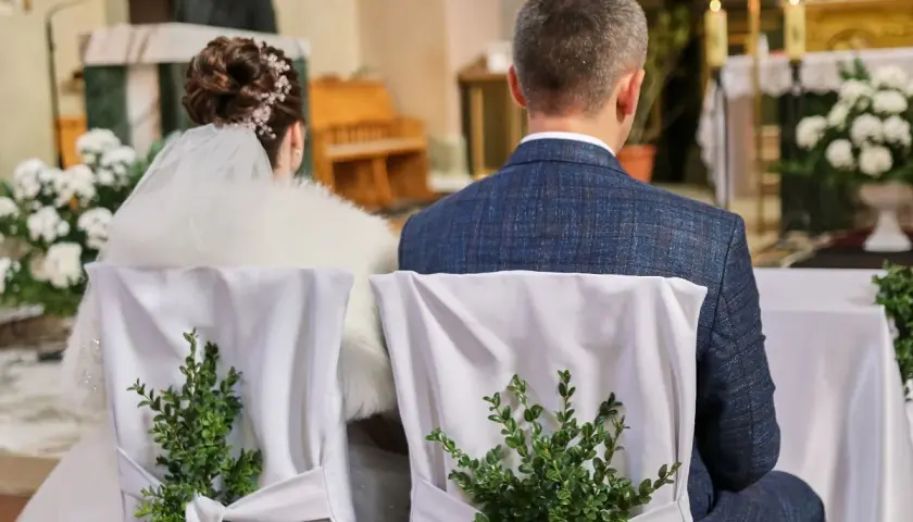 Para młoda siedzi w kościele. Krzesła ozdobione zielonymi gałązkami. Kto nie może być świadkiem na ślubie kościelnym?