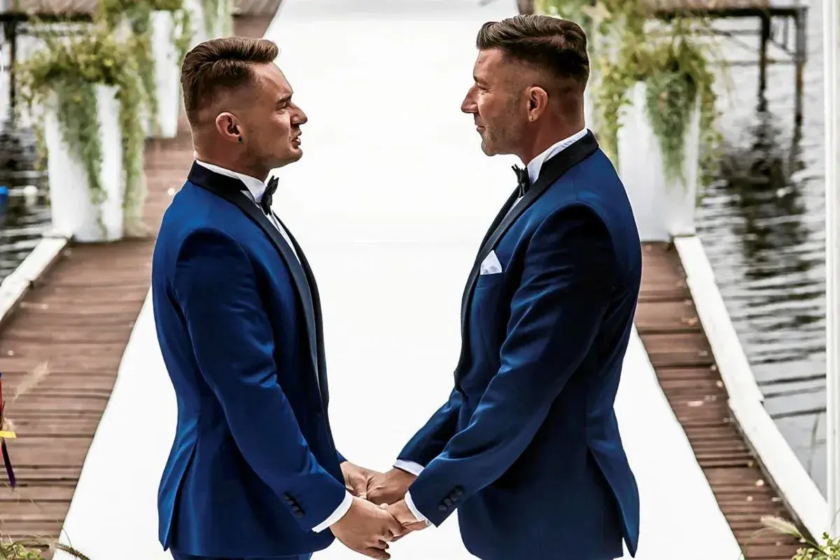 Dwóch panów w eleganckich garniturach trzyma się za ręce, celebrując swój ślub homoseksualny.