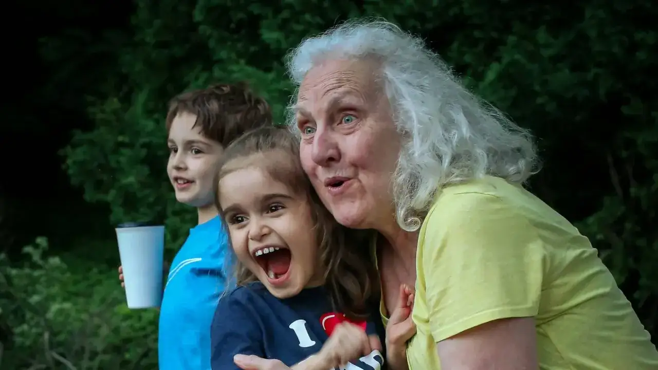 Babcia i wnuczka śmieją się radośnie na tle zieleni. Wnuczek trzyma kubek.