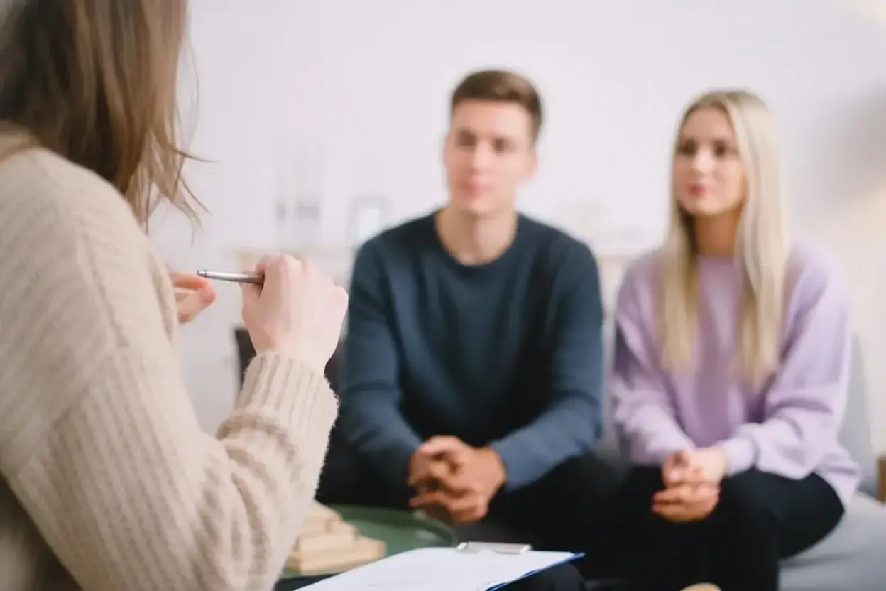 Terapia par: młode małżeństwo pracuje nad dystansem emocjonalnym w związku, słuchając uważnie terapeuty.