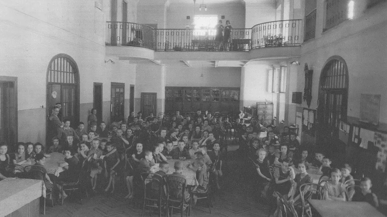 Dzieci w dużej sali, jakby słuchały mądrych korczak cytaty o dzieciach. W tle widać piętrową galerię.